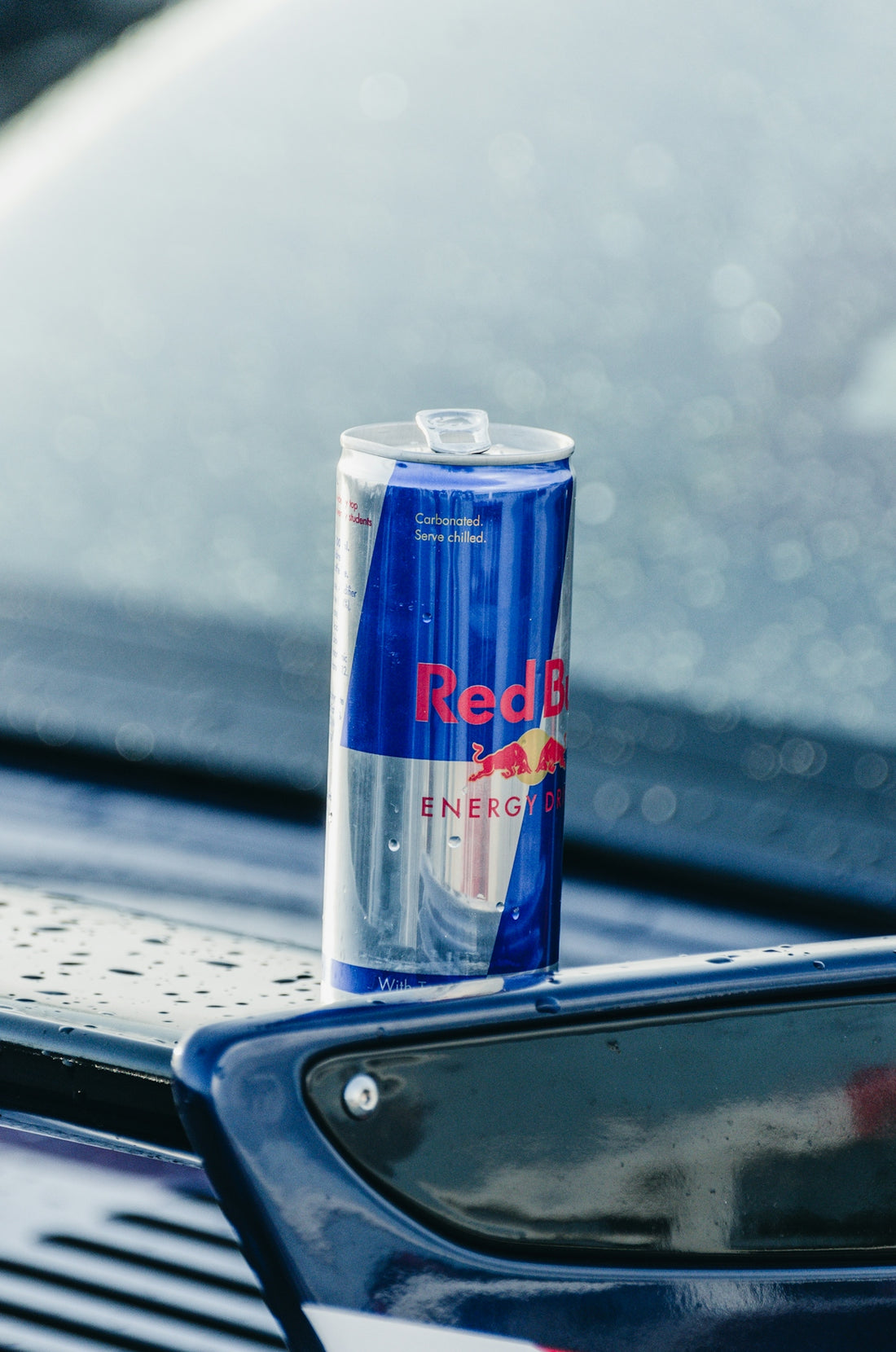 A can of red bull is sitting on the hood of a car